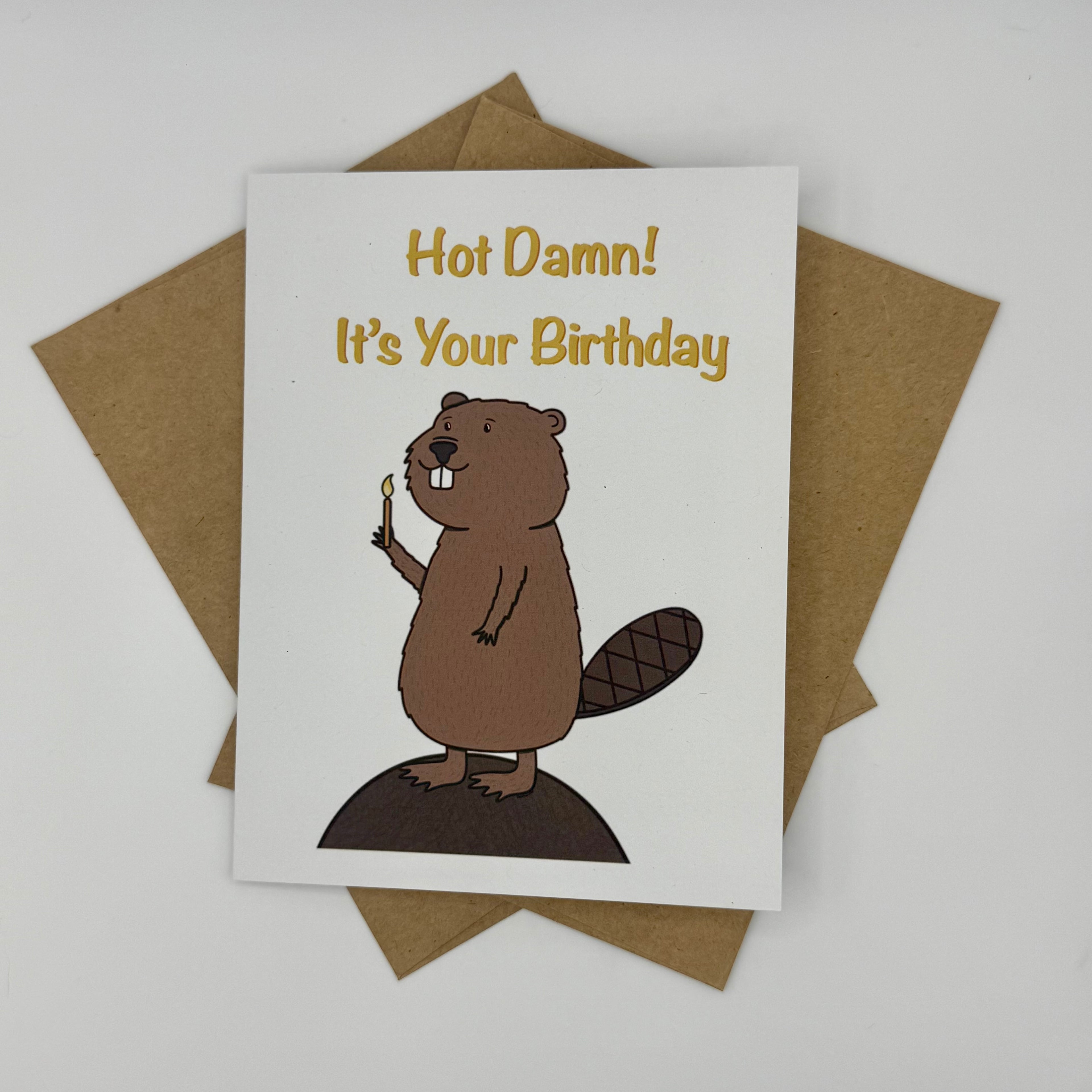 Birthday card with a beaver illustration and 'Hot Damn! It's Your Birthday' text, placed on a brown envelope.