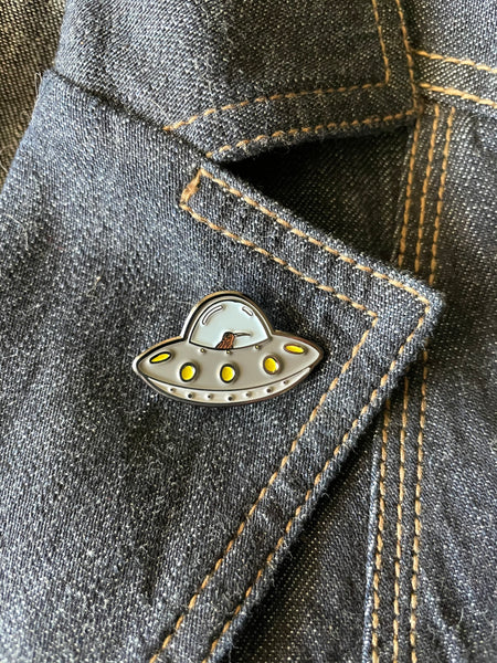 kiwi bird in a flying saucer enamel pin. small grey flying saucer with a kiwi at the helm- pin has texture and no resin coating